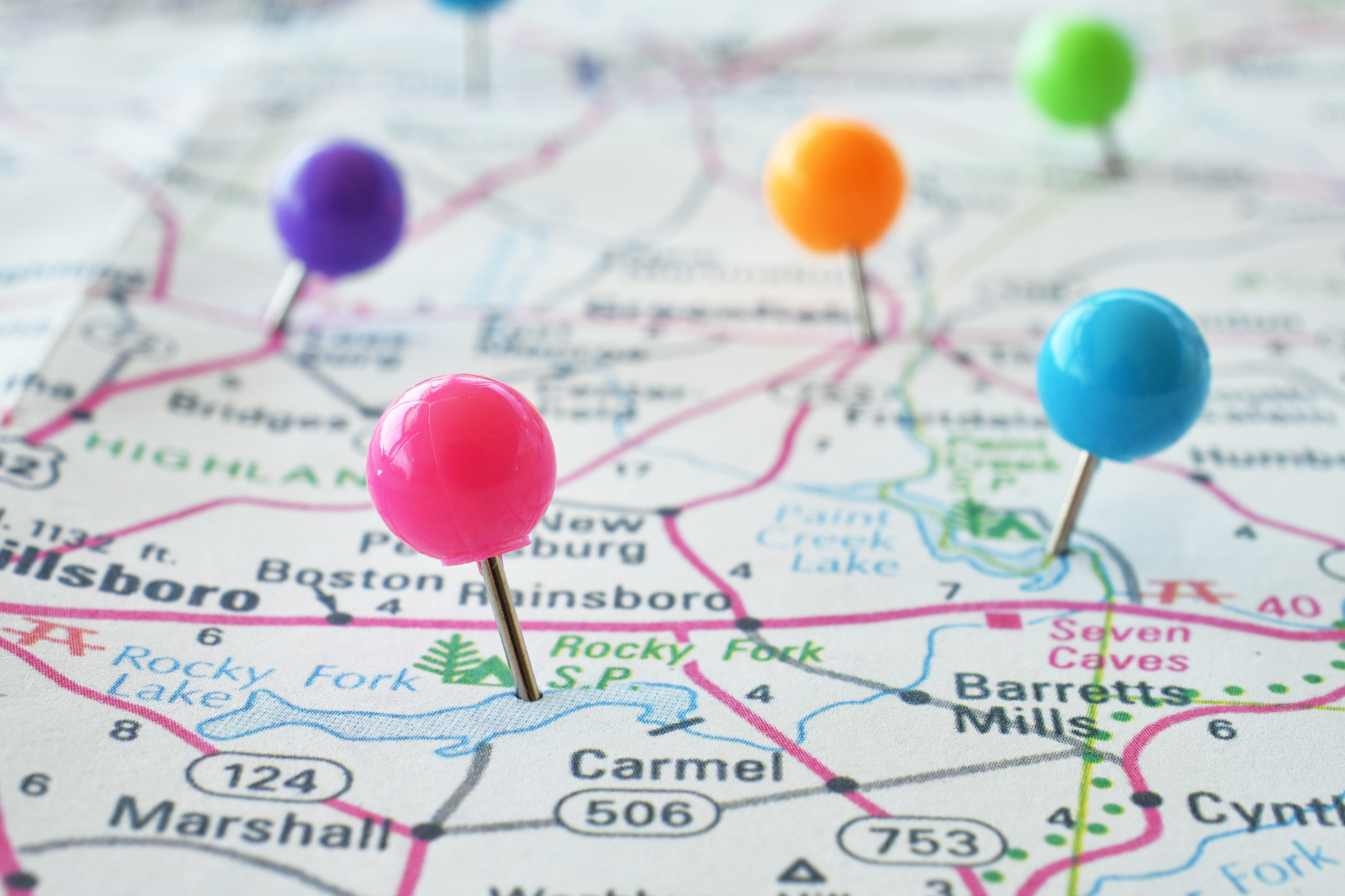 Colorful push pins marking locations on a printed road map of towns and highways